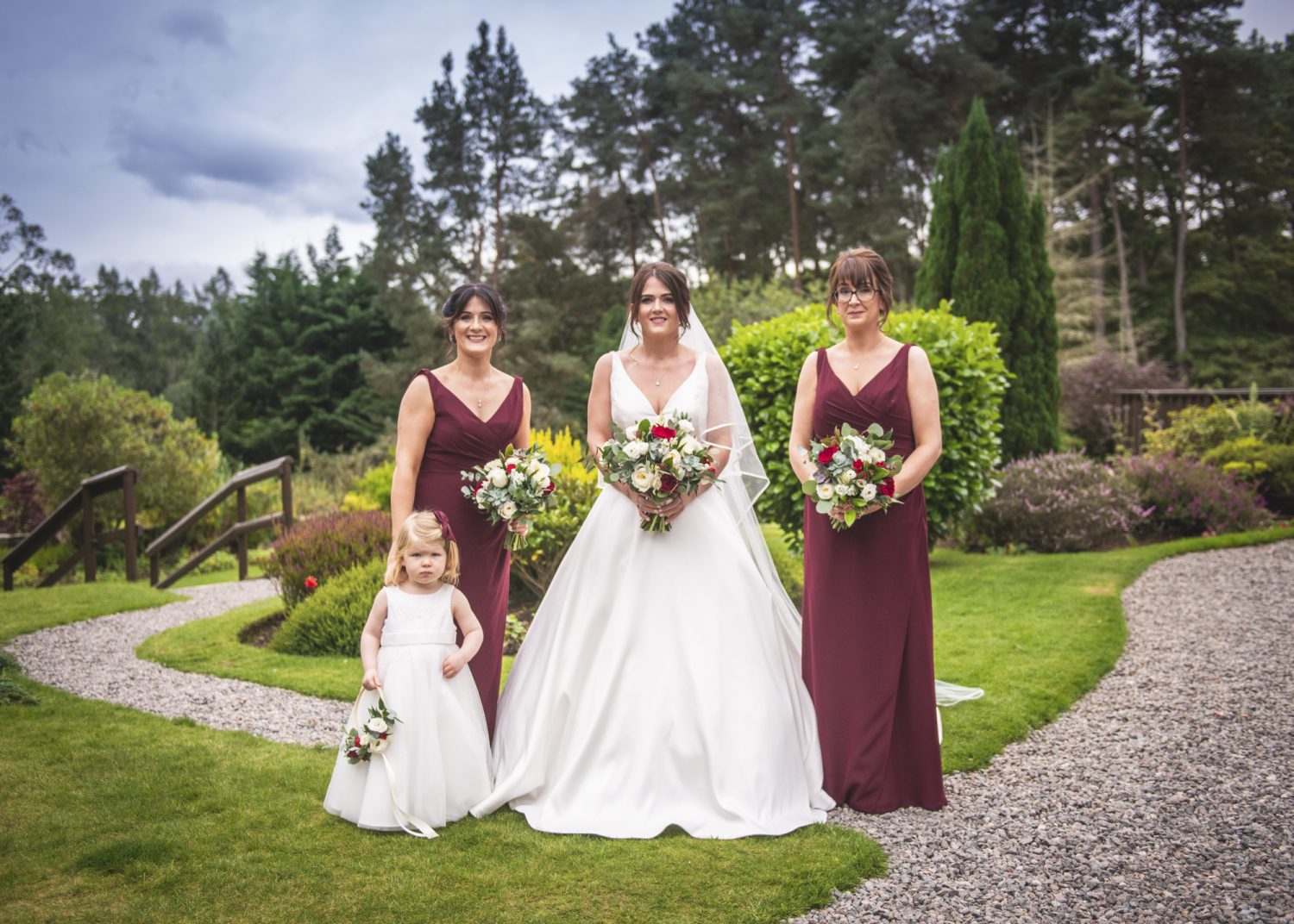Bride, bridesmaids and flower girl standing in hotel grounds
