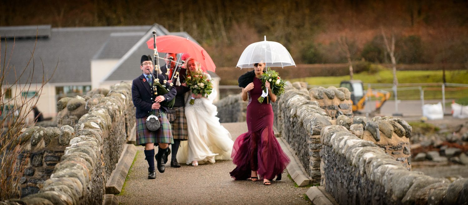 Bridal party led by a piper make their way across the bridge for their Eilean Donan Castle wedding